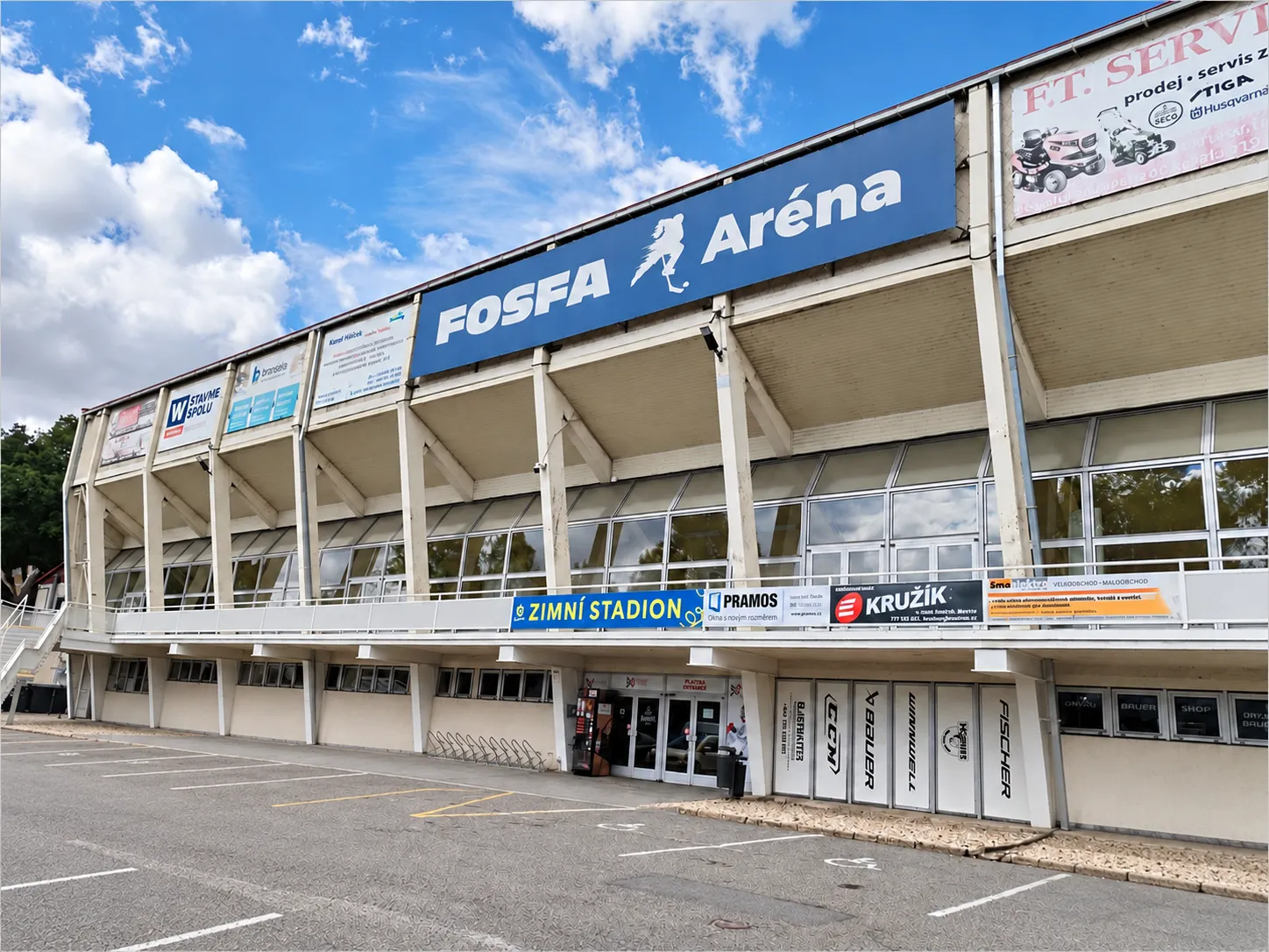Dlouhé průčelí Zimního stadionu v Břeclavi pod nápisem FOSFA Aréna, s parkovištěm a vchodem pod tribunou – Zimní stadion Břeclav
