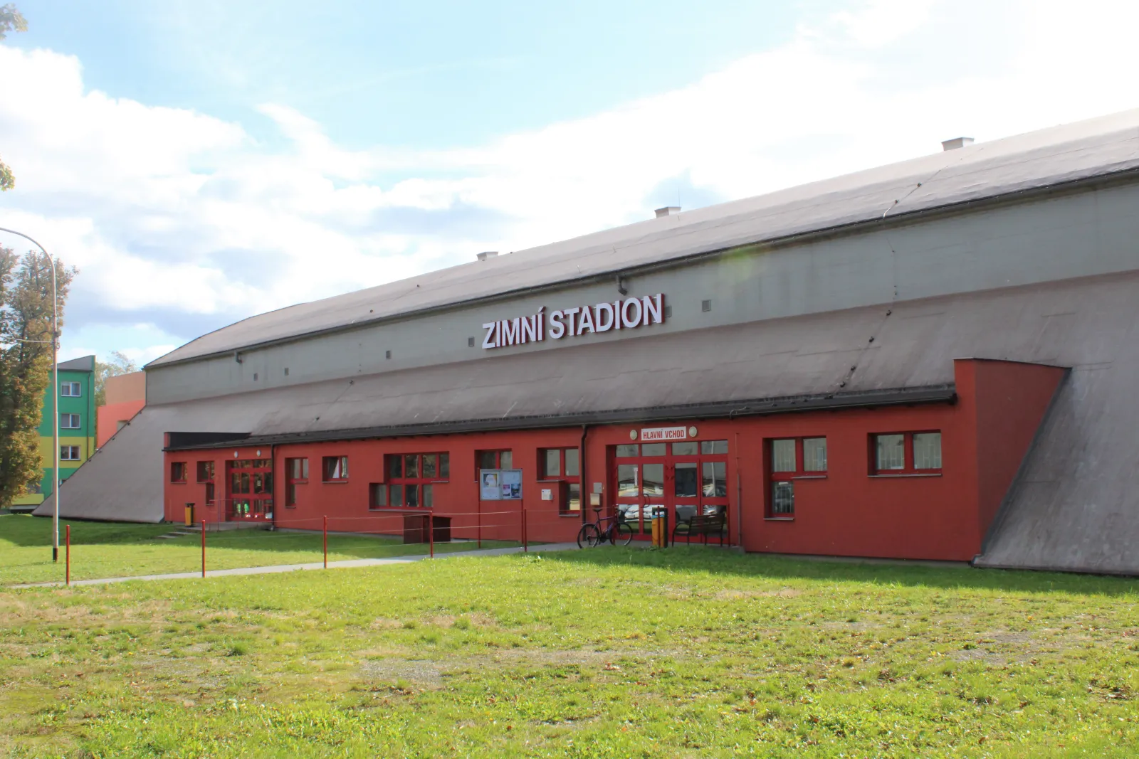 The front of the Český Těšín winter stadium: a long curved-roof hall with the words ZIMNÍ STADION on its red entrance building, seen across the grass. — Zimní stadion Český Těšín
