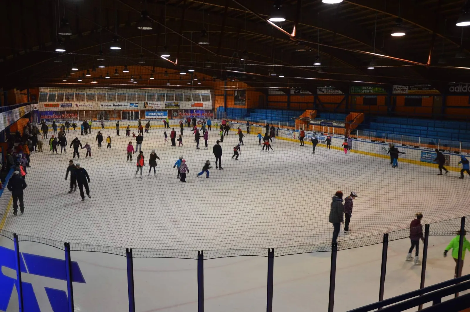 A crowded public session at the Jablonec winter stadium, skaters spread across the whole ice under the lamps and the timber roof. — Zimní stadion Jablonec nad Nisou