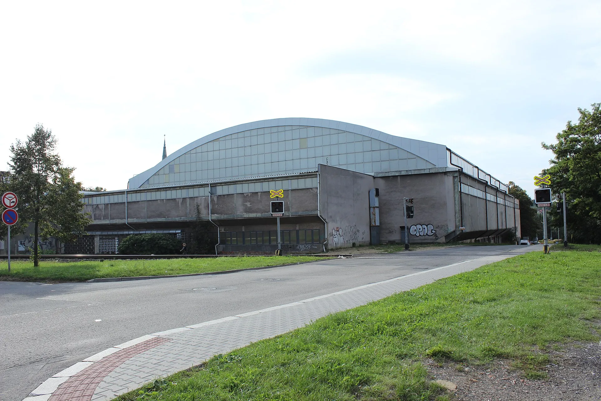 Zimní stadion v Kopřivnici z ulice, s obloukovou prosklenou střechou nad betonovou halou – Zimní stadion Kopřivnice