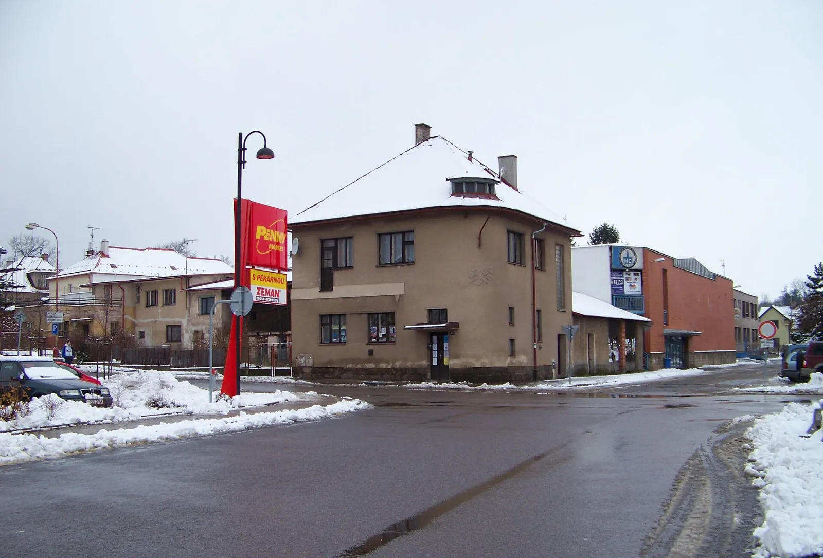 The brick-clad side of the Lomnice nad Popelkou ice stadium with the club's HC emblem and sponsor banners above the entrance stairs. – Zimní stadion Lomnice nad Popelkou