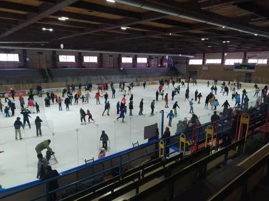 A public-skating session at the Mariánské Lázně ice stadium, with skaters filling the ice sheet under the timber roof and the stands behind. – Zimní stadion Mariánské Lázně
