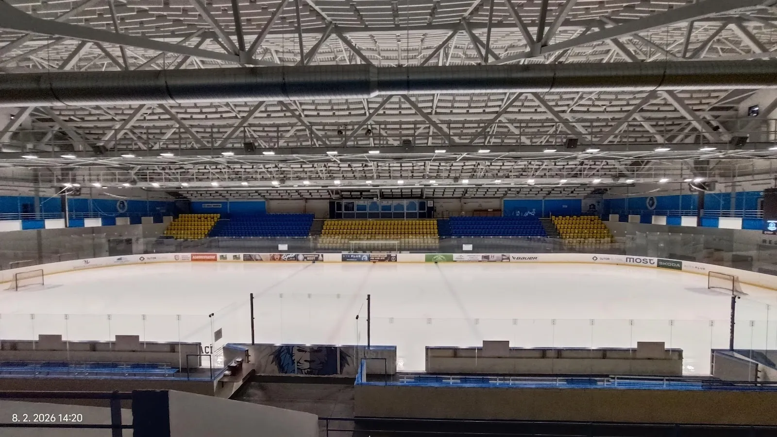 Led zimního stadionu v Mostě z tribuny, s ocelovou střechou a řadami sedadel kolem kluziště. – Zimní stadion Most