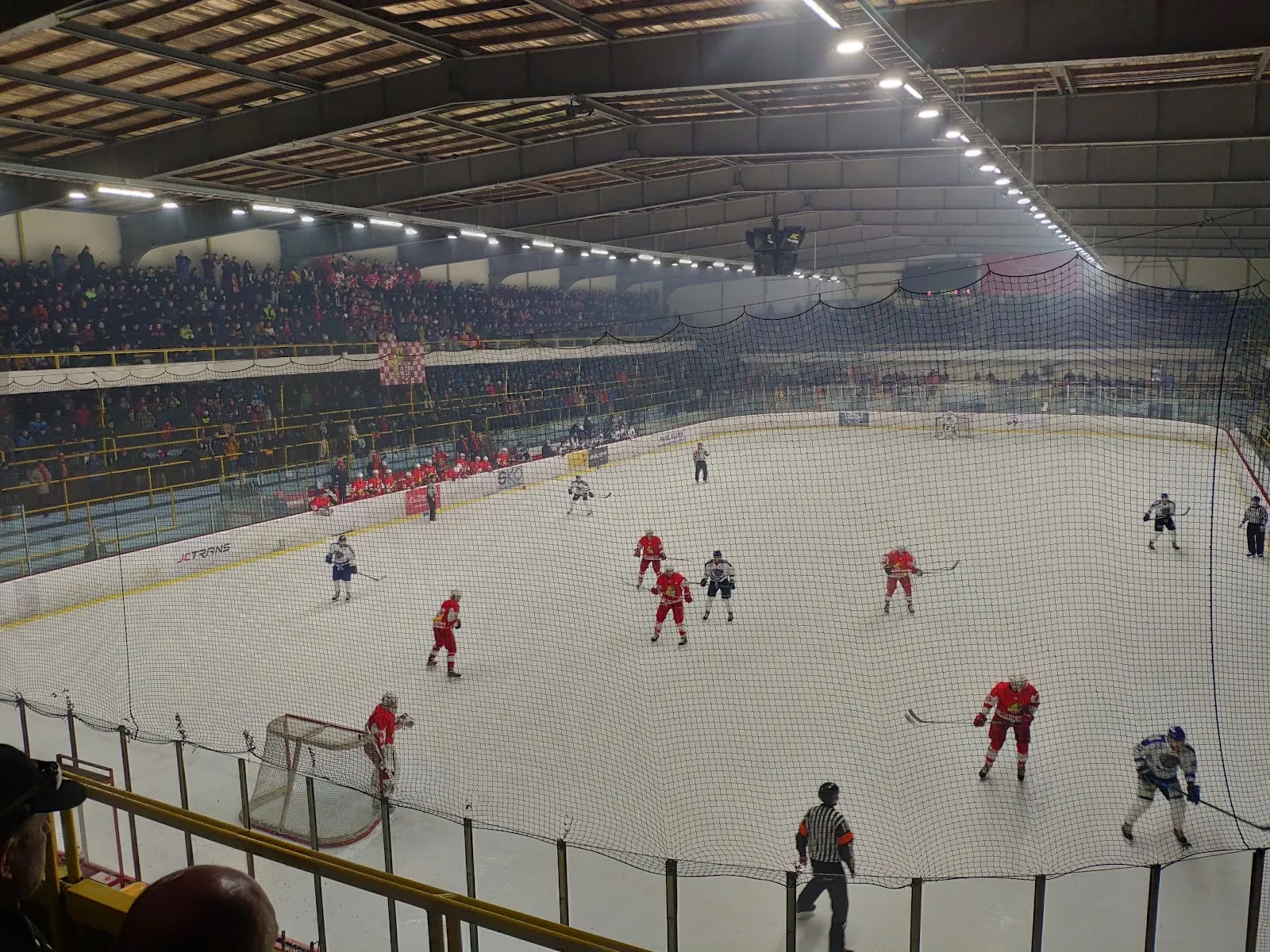 Zápas na ledě zimního stadionu v Opavě, pohled z tribuny přes mantinely, nad hrací plochou osvětlení střechy. – Zimní stadion Opava (Slezan Aréna)