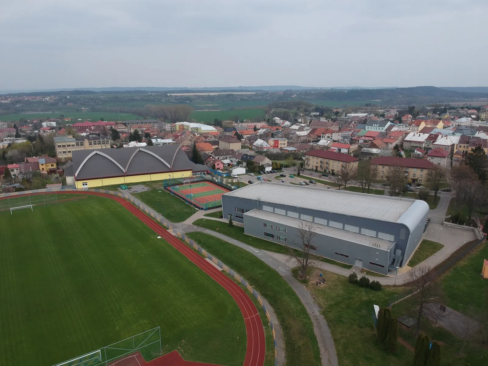 Letecký pohled na Skuteč se zimním stadionem s obloukovou střechou vlevo vedle sportovní haly a fotbalového hřiště – Zimní stadion Skuteč