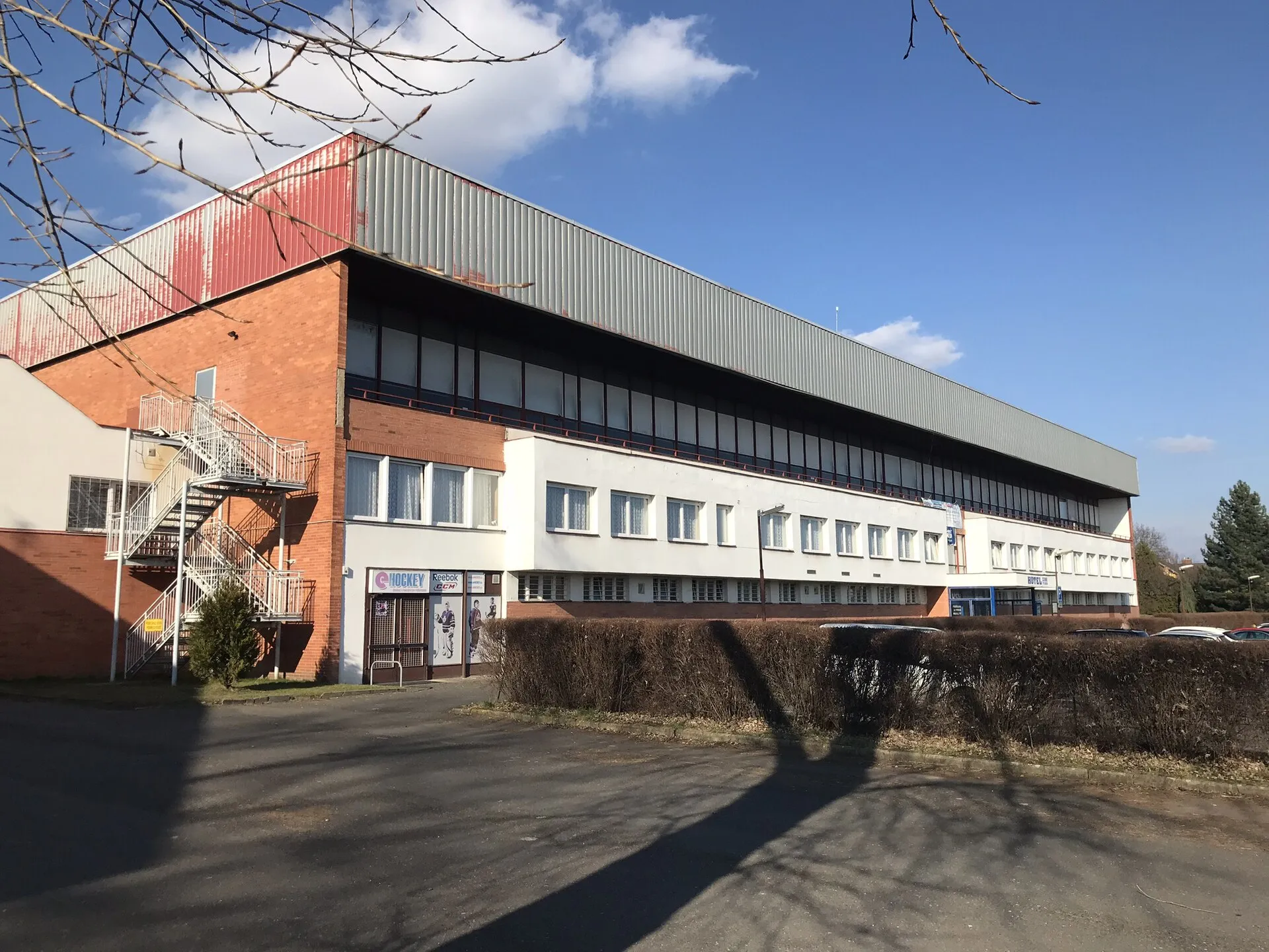 The long side of the Zimní stadion in Slaný in 2018, with the brick end, the white upper floor and the sloping roof — Zimní stadion Slaný