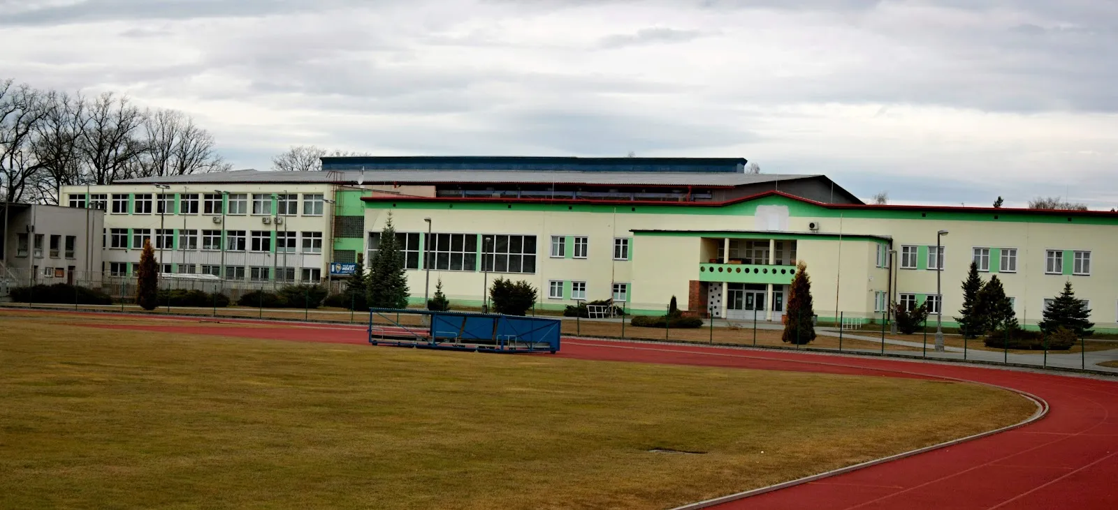 The pale green-roofed Soběslav winter stadium building seen across a running track and lawn. — Zimní stadion Soběslav