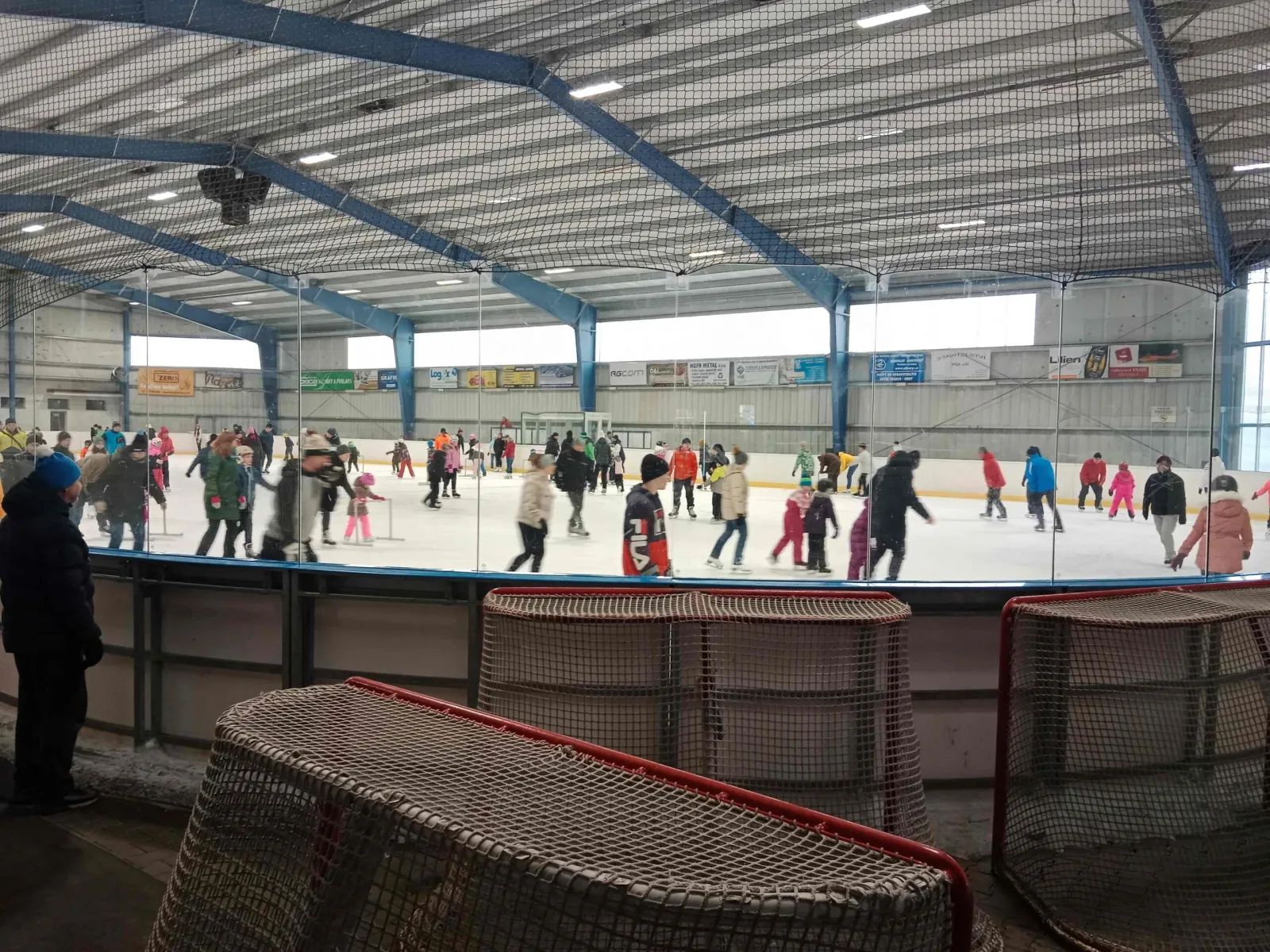 A public-skating session at the stadium, with skaters of all ages across the ice behind the glass and the steel-framed roof overhead. — Zimní stadion Třebechovice pod Orebem