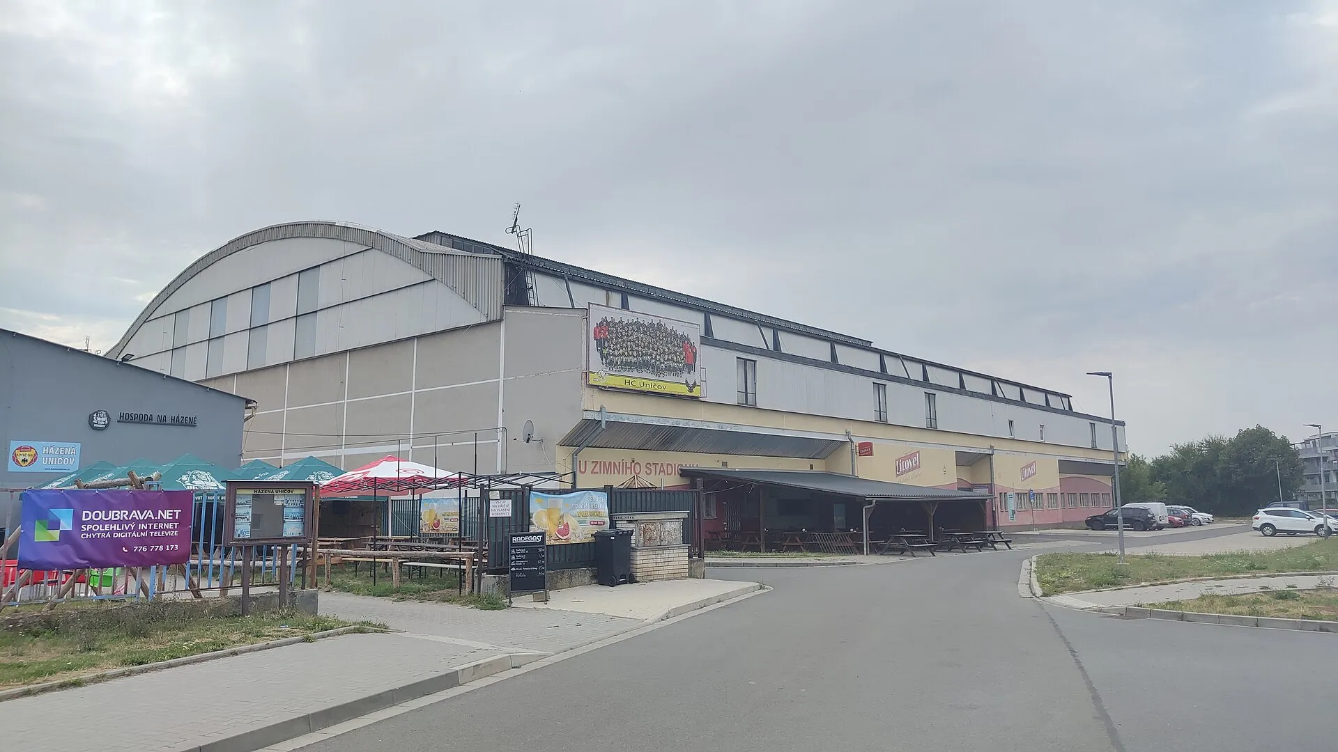 The arched roof and front of the Zimní stadion in Uničov with the entrance sign and the outdoor seating of the bar beside it — Zimní stadion Uničov