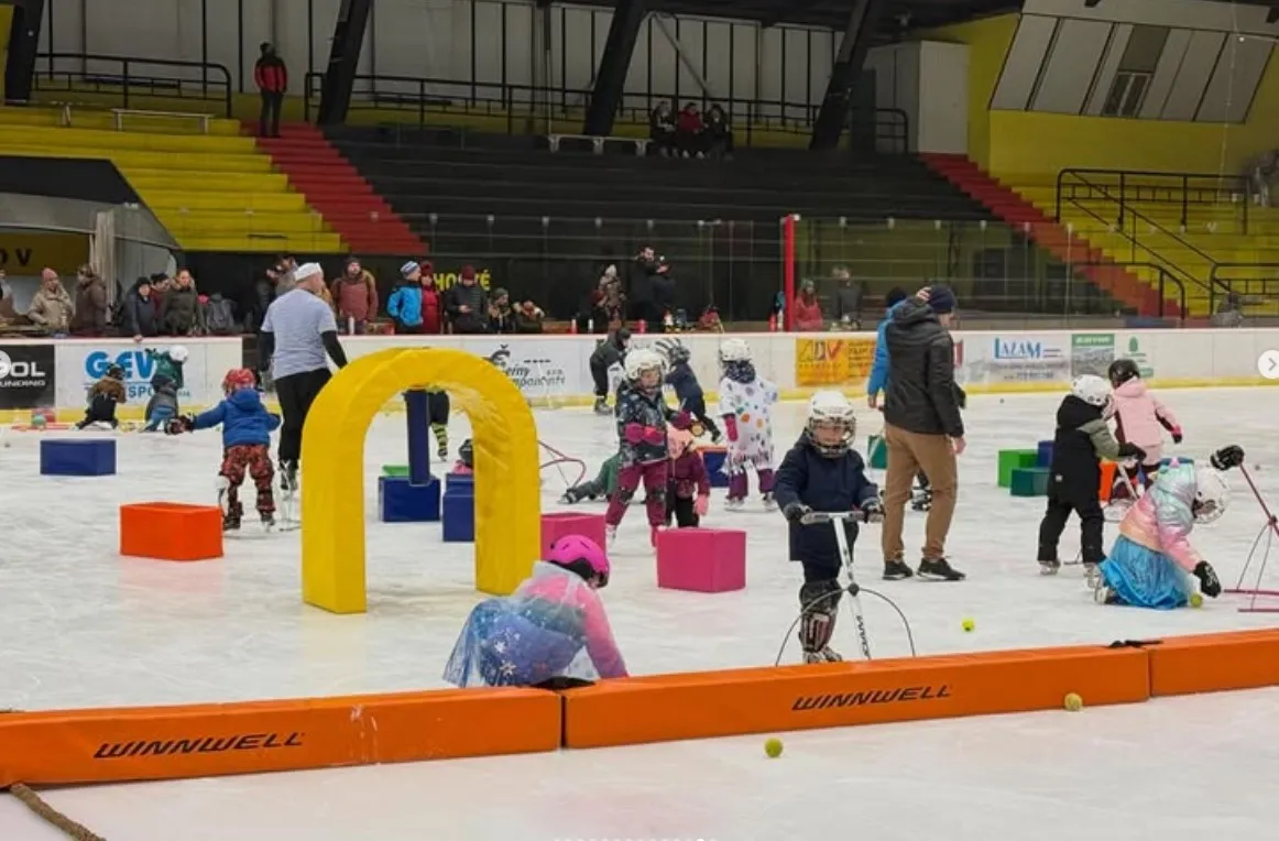Children on the ice of the Zimní stadion in Uničov during a skating-school event, with play equipment on the ice and the yellow and black stands behind — Zimní stadion Uničov