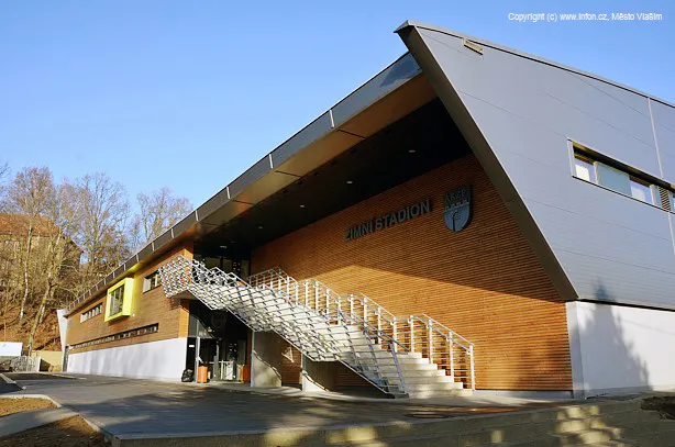 Vlašimský zimní stadion zvenčí: dřevem obložená hala s nápisem ZIMNÍ STADION nad ocelovým schodištěm ke vchodu. – Zimní stadion Vlašim