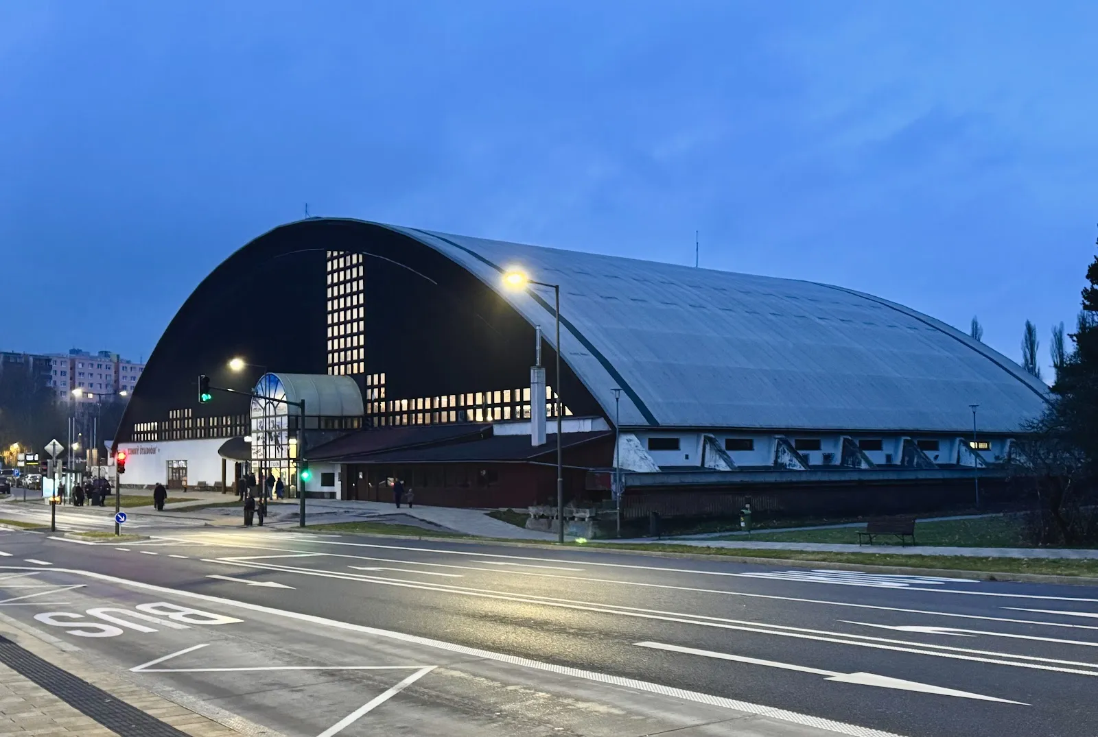 The arched roof of Zimný štadión Harmincova at dusk, seen from the street — Zimný štadión Harmincova