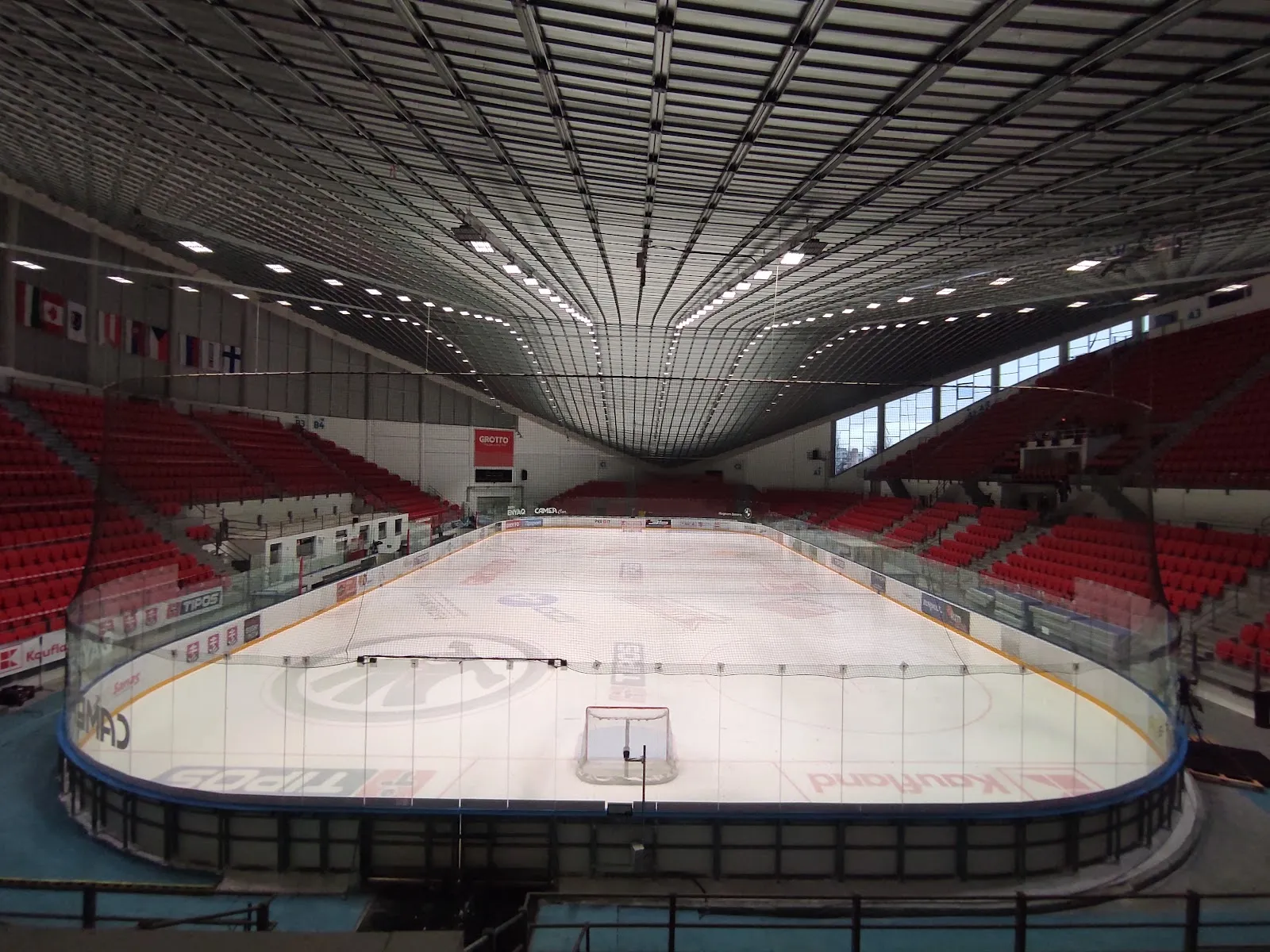 The empty ice sheet of the Zimný štadión in Prešov seen from the stands, with red seating and the lighting rig under the roof — Zimný štadión Prešov